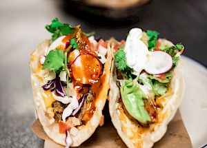 The image shows two tacos filled with various ingredients, such as meat, vegetables, and garnishes, on a plate placed on a table.