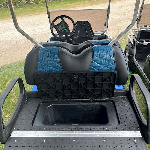 The image shows the rear seat and cargo area of a golf cart. The seat is folded forward, exposing a storage compartment underneath.