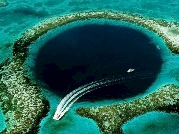 The image shows the Great Blue Hole, a large underwater sinkhole off the coast of Belize, with two boats seen near its edge.