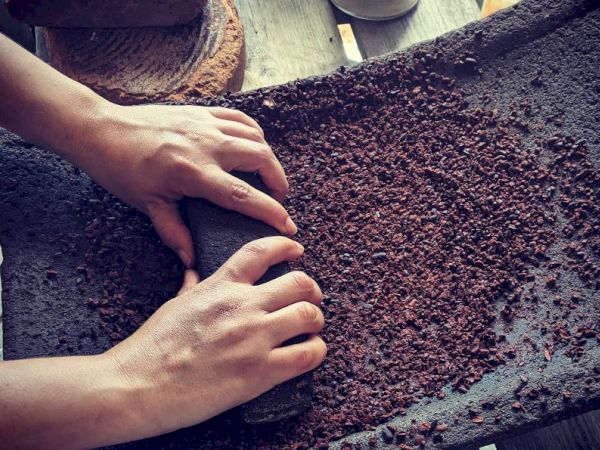Two hands are grinding what appears to be cocoa beans on a traditional stone grinding surface.